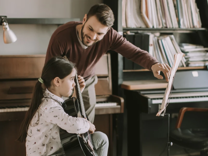 Music teacher guiding a young student with notation on a music stand