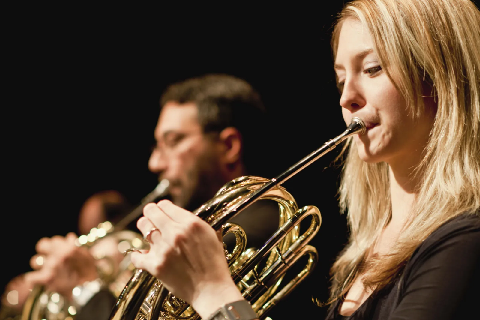 French horn players performing together on a darkened concert stage.