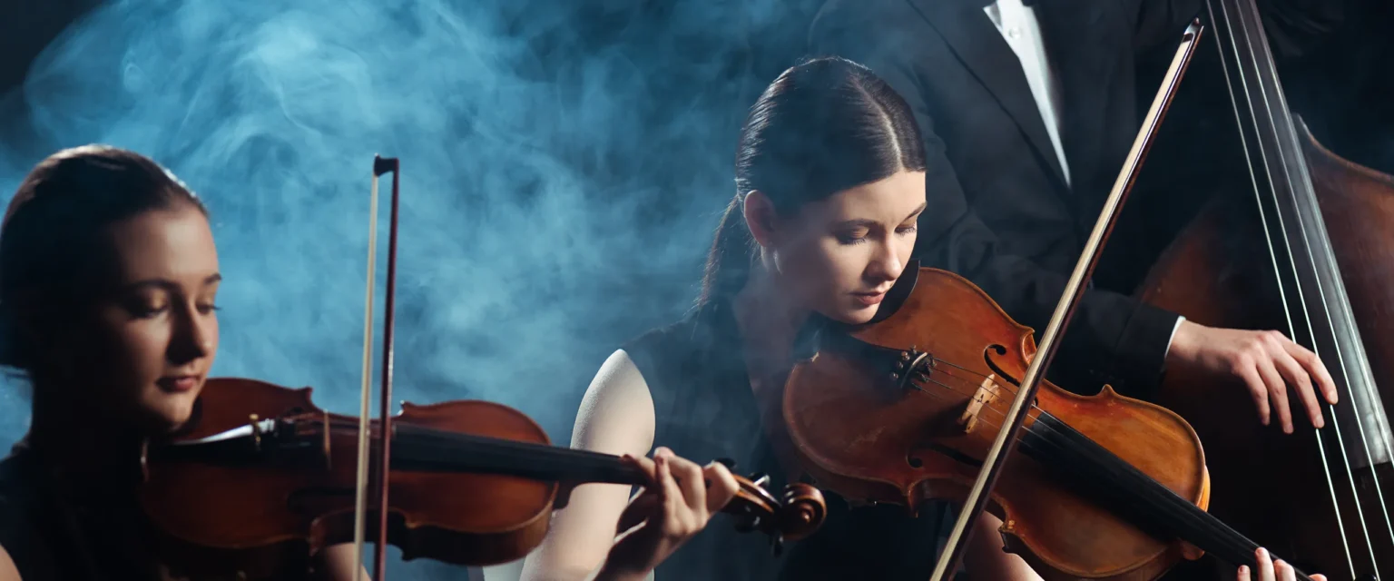 String players performing together under warm stage light.
